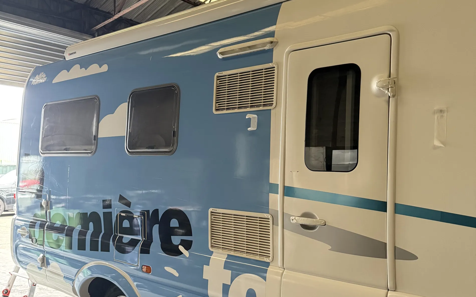 Pose du covering en cours sur le camping-car Radio Nova : véhicule à moitié habillé dans l'atelier
