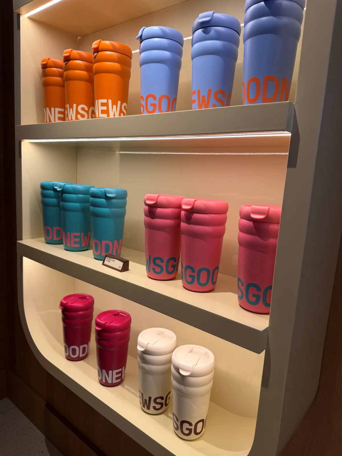 Mugs GoodNews personnalisés de stickers en vinyle, présentés en rayon dans un coffee shop parisien